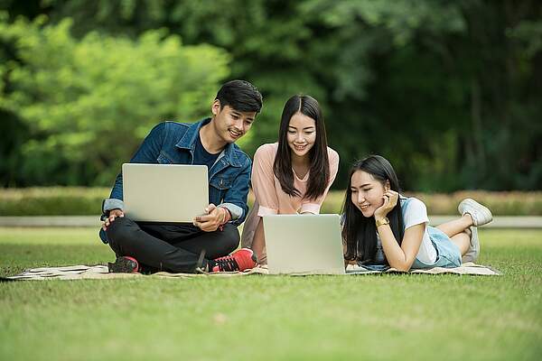 Drei Personen sitzen mit Laptop auf einer Wiese