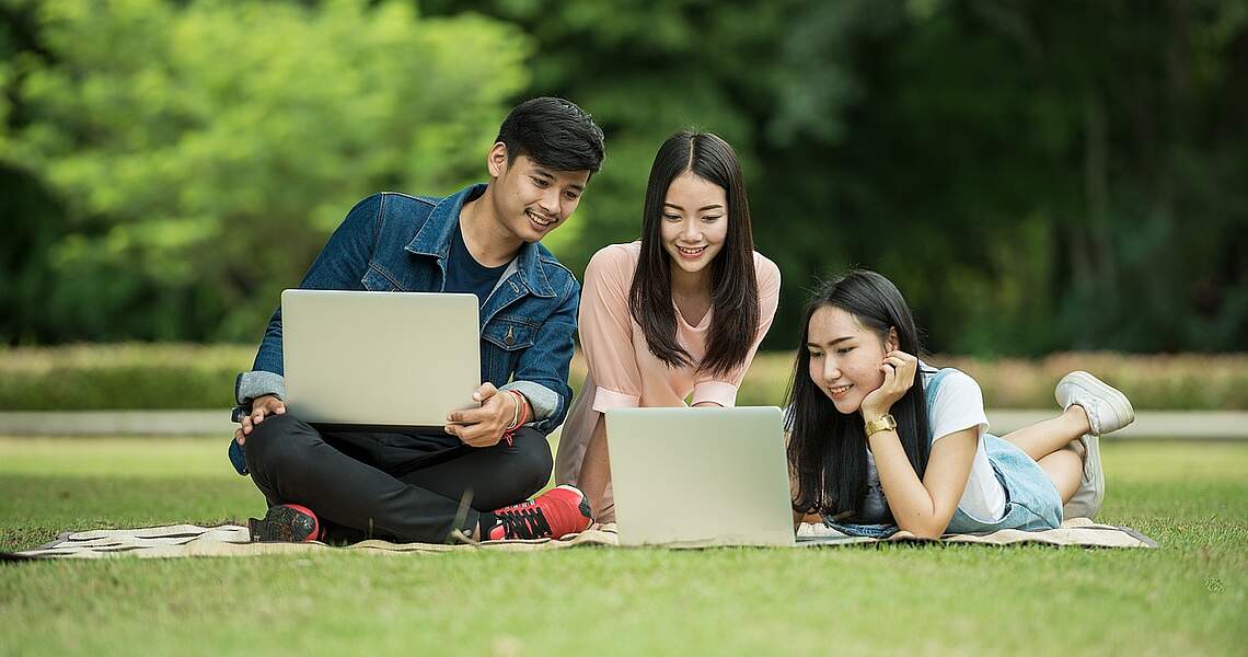 Drei Personen sitzen mit Laptop auf einer Wiese Drei Personen sitzen mit Laptop auf einer Wiese
